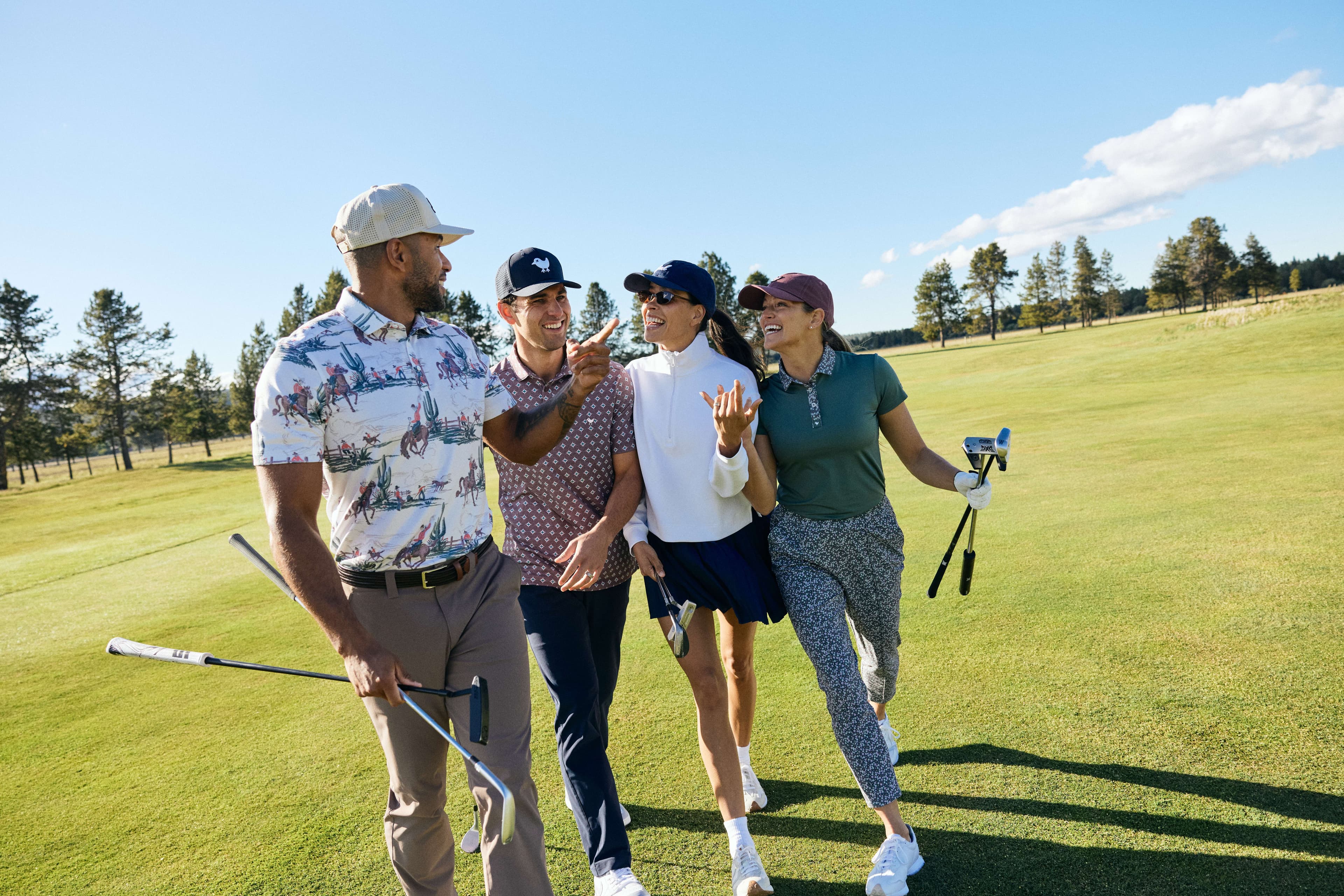 Four people walking together on Meadows golf course, smiling and holding golf clubs, wearing casual golf attire on a sunny day with trees and blue sky in the background.