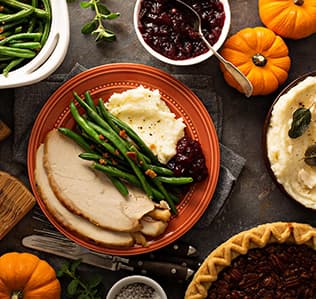A Thanksgiving meal with turkey, green beans, mashed potatoes, cranberry sauce, a pecan pie, mini pumpkins, and bowls of sides, arranged on a wooden table.