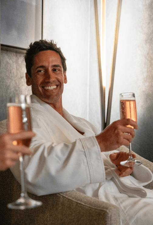 Guest in a white robe relaxing with a glass of sparkling wine in a tranquil spa lounge.